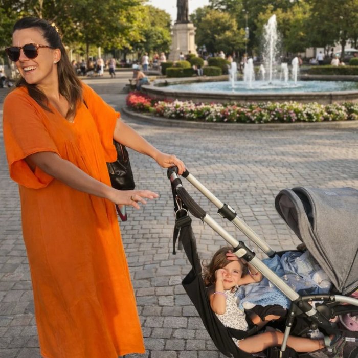 Mamá con vestido naranja paseando con coche doble en plaza