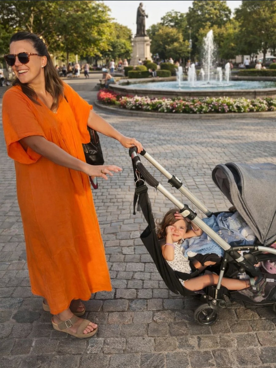 Mamá paseando con la hamaca Pepe Pillo en una plaza, niña sonriente disfrutando el paseo